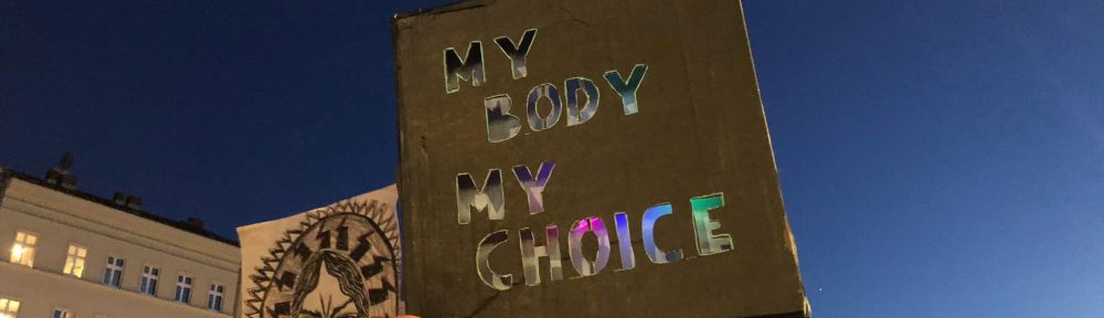 Foto. Ein Arm hält ein Schild hoch, auf diesem steht: My Body my Choice.
